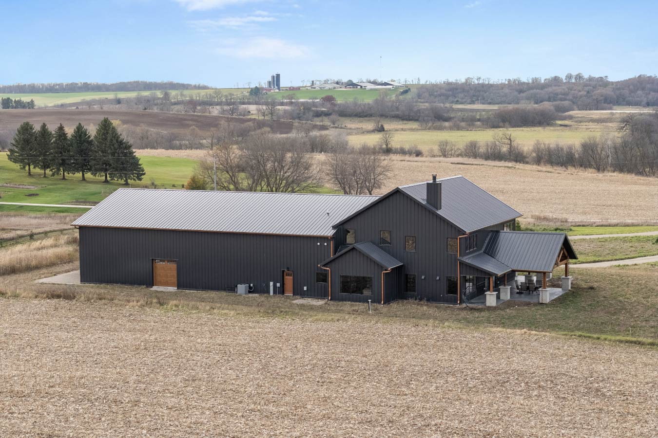 The rear of the barndominium highlights its expansive design, surrounded by rolling fields and natural beauty.