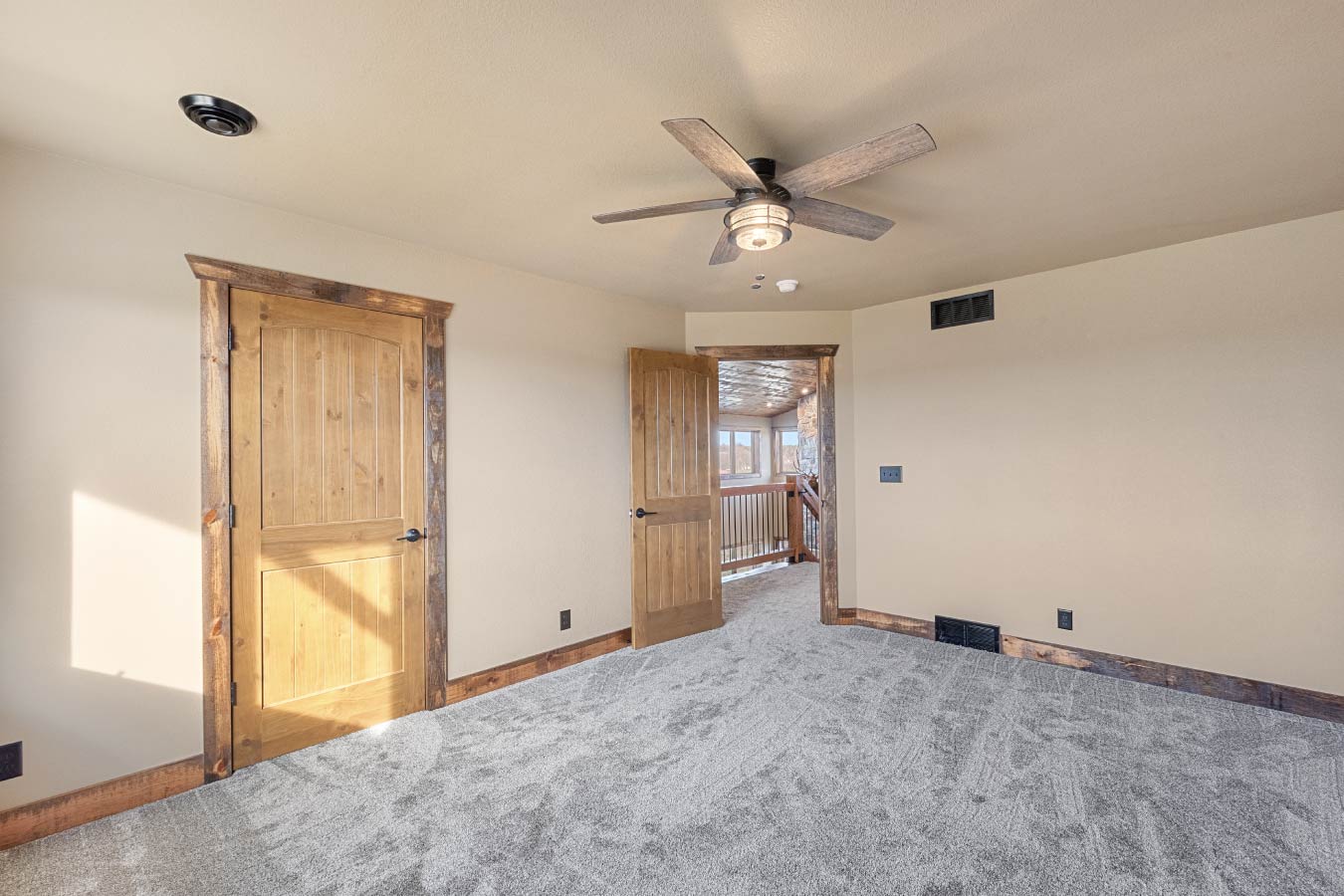A secondary bedroom in the Barndominium with Workshop featuring rustic wooden doors and a ceiling fan for comfort and style.