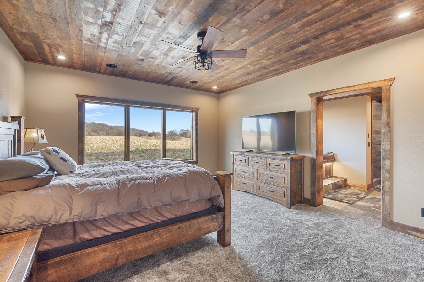 A spacious master bedroom with a wooden ceiling, large windows, and warm natural light.