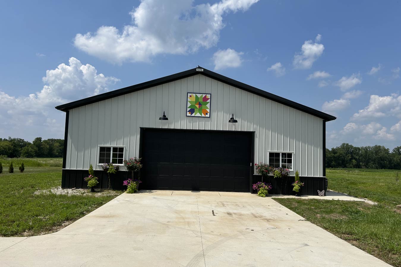 The front elevation features a black overhead door framed by clean two-tone steel siding.